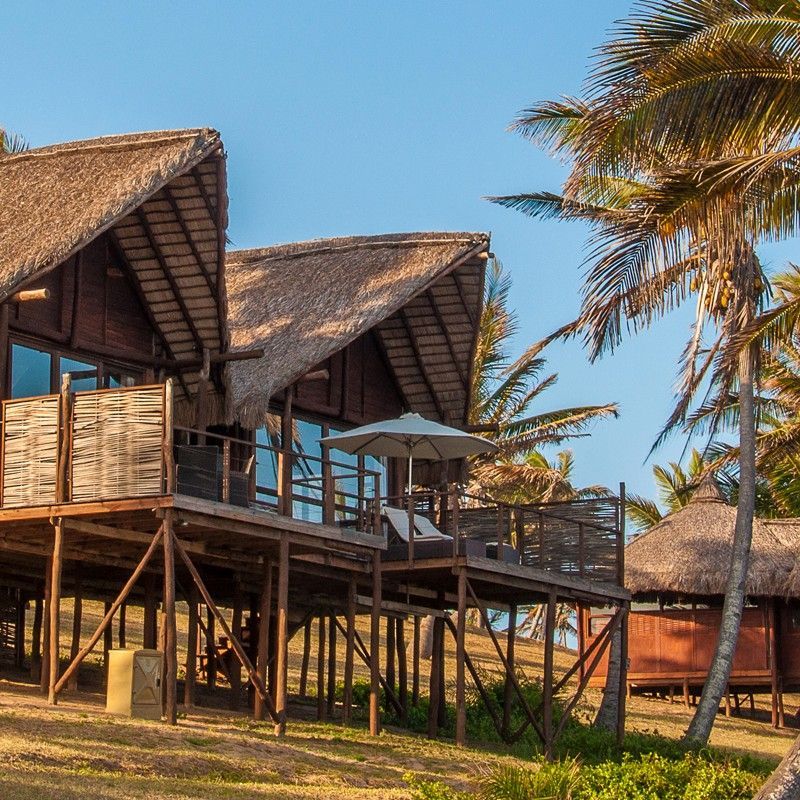 The exterior of the chalets at Massinga Beach in Mozambique is captured in this inviting travel photograph, showcasing rustic yet comfortable beachfront accommodation set amid swaying palms and tropical greenery. Thatched roofs and natural wooden structures blend harmoniously with the sandy surroundings, creating a sense of simplicity and connection to the coastline. Each chalet features private outdoor spaces or decks that open toward the ocean, inviting guests to enjoy unobstructed views of the turquoise waters and pristine beach. The scene conveys tranquility, relaxed coastal living, and an immersive seaside experience, highlighting Massinga Beach as an idyllic retreat for those seeking natural beauty and laid-back charm. Inspiration Africa specializes in bespoke, tailor-made journeys to Mozambique and across Africa, crafting unforgettable travel experiences in extraordinary destinations.
