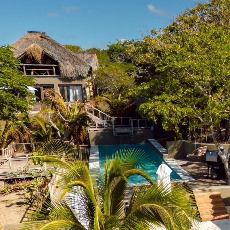 The swimming pool at Mozawi Beach Lodge in Mozambique is captured in this striking aerial travel photograph, showcasing the pool set within lush tropical gardens and framed by golden sandy beaches. The pool’s turquoise waters mirror the nearby Indian Ocean, creating a seamless visual connection between the lodge and the coastline. Sun loungers and shaded areas around the pool invite relaxation, while the surrounding greenery enhances the sense of privacy and immersion in nature. The scene conveys tranquility, seaside luxury, and harmony with the natural environment, highlighting Mozawi Beach Lodge as a serene coastal retreat in Mozambique. Inspiration Africa specializes in bespoke, tailor-made journeys to Mozambique and across Africa, crafting unforgettable travel experiences in extraordinary destinations.
