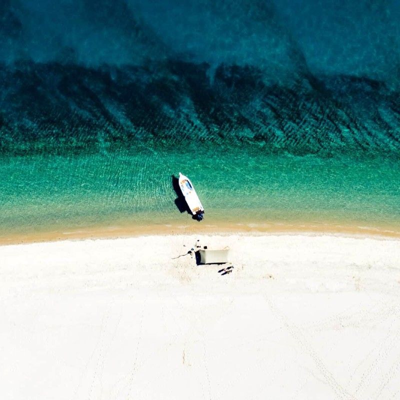 Witness the stunning convergence of elements in the Bazaruto Archipelago, Mozambique. This aerial view showcases a pristine, solitary strip of white sand, dramatically defined by the surrounding ocean. The water shifts beautifully, moving from brilliant, bright turquoise near the edge to a rich deep ocean blue further out. Inspiration Africa specializes in designing your exclusive, tailor-made trip to Mozambique's aquatic wonders and other spectacular destinations across Africa. Plan your private island escape with us!