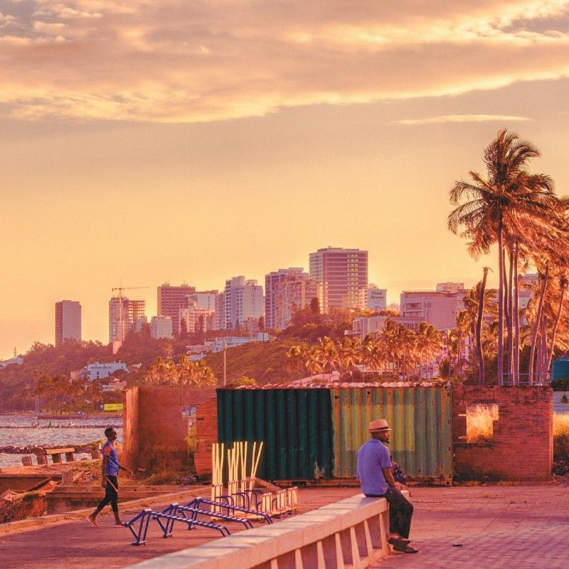 Maputo, Mozambique, is captured in this atmospheric travel photograph during a beautiful pink sunset, as soft pastel hues wash over the city skyline and coastline. The warm glow of the fading sun reflects off buildings, streets, and the ocean beyond, creating a tranquil yet vibrant mood. Silhouettes of palm trees and urban landmarks stand out against the colorful sky, blending coastal charm with the energy of the capital. The scene conveys romance, warmth, and a sense of place, highlighting Maputo as a city where culture, ocean views, and unforgettable sunsets come together. Inspiration Africa specializes in bespoke, tailor-made journeys to Mozambique and across Africa, crafting unforgettable travel experiences in extraordinary destinations.
