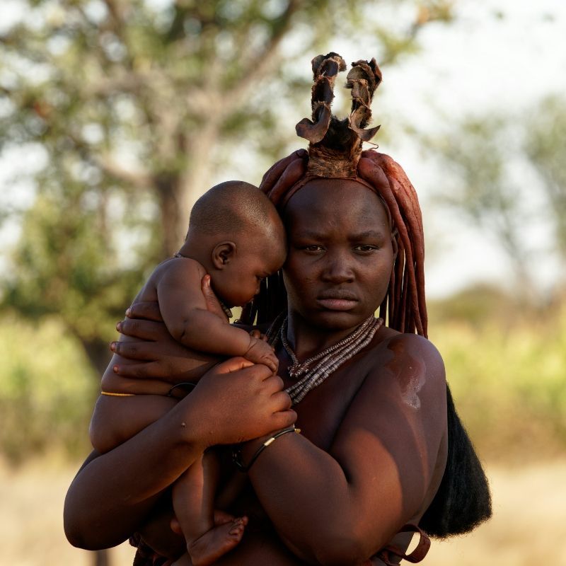 This poignant portrait features a beautiful Himba woman from Namibia, dressed in her distinctive traditional clothes and makeup. She holds a baby tenderly while gazing calmly into the distance, embodying the grace and resilience of her people. Inspiration Africa specializes in designing your unique, tailor-made trip to Namibia for authentic cultural experiences and exploring other extraordinary destinations across Africa. Discover the rich heritage of Southern Africa with us!