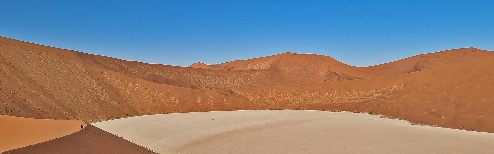 Dead Vlei's striking white clay pan in Namibia's Namib Desert, surrounded by towering red dunes creating an otherworldly, starkly beautiful landscape.