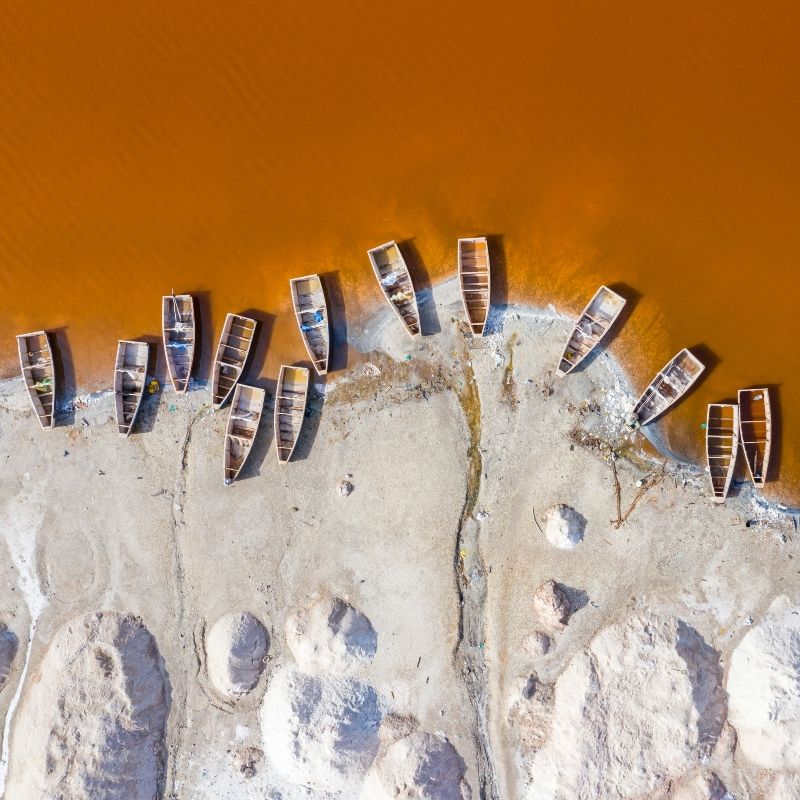 An aerial view of Senegal’s Lac Rose reveals a striking landscape where boats rest along the vivid pink shoreline, shaped by the lake’s high salt content and natural algae. Located northeast of Dakar, Lac Rose is famous for its otherworldly color, traditional salt harvesting, and lively local communities. The contrast between the shimmering water, bright boats, and open sky creates an unforgettable scene. Inspiration Africa offers tailor-made journeys to Senegal, bringing travelers to the heart of Lac Rose and beyond, where vibrant landscapes, culture, and natural beauty come together in one of West Africa’s most unique destinations.
