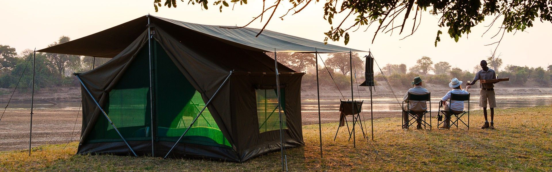 The exterior of a luxury tent at Luangwa Bush Camp by Robin Pope Safaris in South Luangwa National Park, Zambia, is captured in this inviting travel photograph, highlighting its seamless integration with the surrounding wilderness. Elevated on a wooden deck, the tent overlooks open bush and riverine vegetation, offering unobstructed views of the park’s abundant wildlife. Natural materials and neutral tones blend harmoniously with the landscape, emphasizing comfort, style, and a connection to nature. Soft natural light enhances the textures of the canvas, wood, and surroundings, creating a serene and immersive atmosphere. Inspiration Africa curates bespoke, tailor-made journeys to Zambia and across Africa, combining luxury safari accommodations with unforgettable wildlife and nature experiences.
