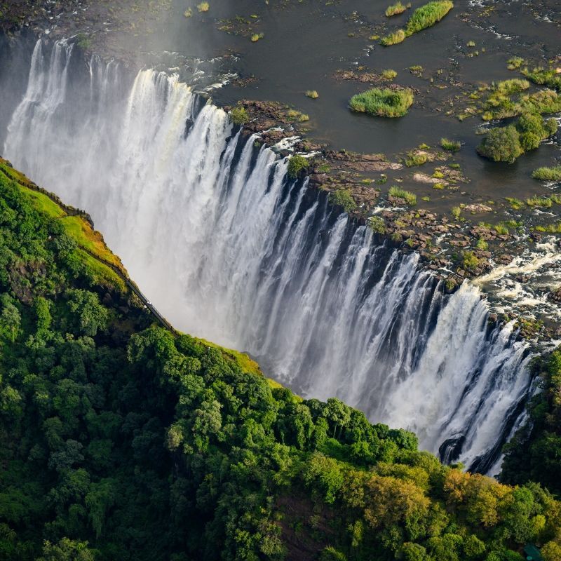 Behold the mighty Victoria Falls, one of Africa’s most impressive natural sights, where powerful waters plunge into the deep Batoka Gorge, sending mist high into the air and surrounded by lush green vegetation. This stunning aerial view captures the immense scale of 