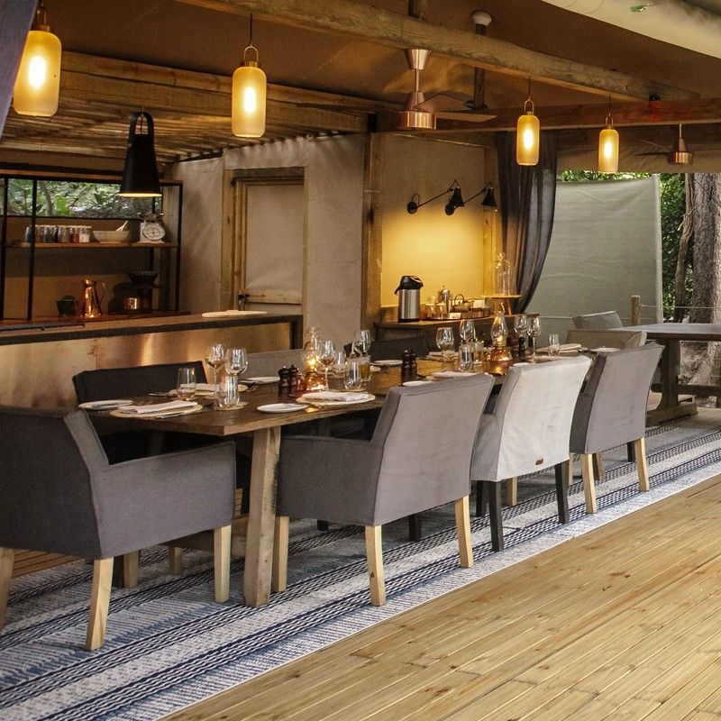 The dining area at Tsowa Safari Island in Zimbabwe is featured in this atmospheric travel photograph, set on a secluded island along the Zambezi River. An open-air dining space with natural wooden furnishings and a thatched or canvas canopy creates a relaxed yet intimate setting, allowing guests to enjoy meals surrounded by riverine vegetation and the sounds of nature. Soft lighting and carefully arranged tables enhance the sense of exclusivity and connection to the wilderness. The scene reflects the lodge’s authentic safari style, combining comfort with a close relationship to the surrounding environment. Inspiration Africa specializes in bespoke, tailor-made journeys to Zimbabwe and across Africa, crafting unforgettable safari experiences in extraordinary wilderness destinations.
