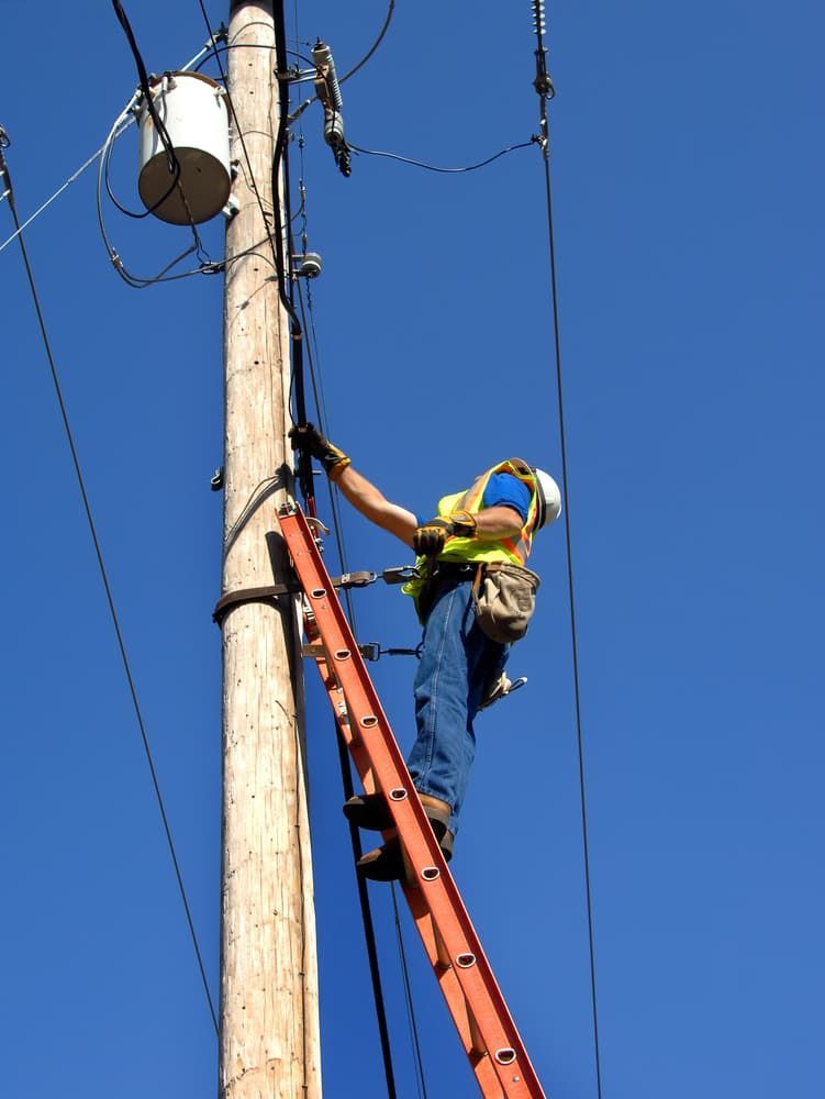 A Man on a Ladder is Working on a Power Pole — Joyner Electrical Pty Ltd In Carrara, QLD
