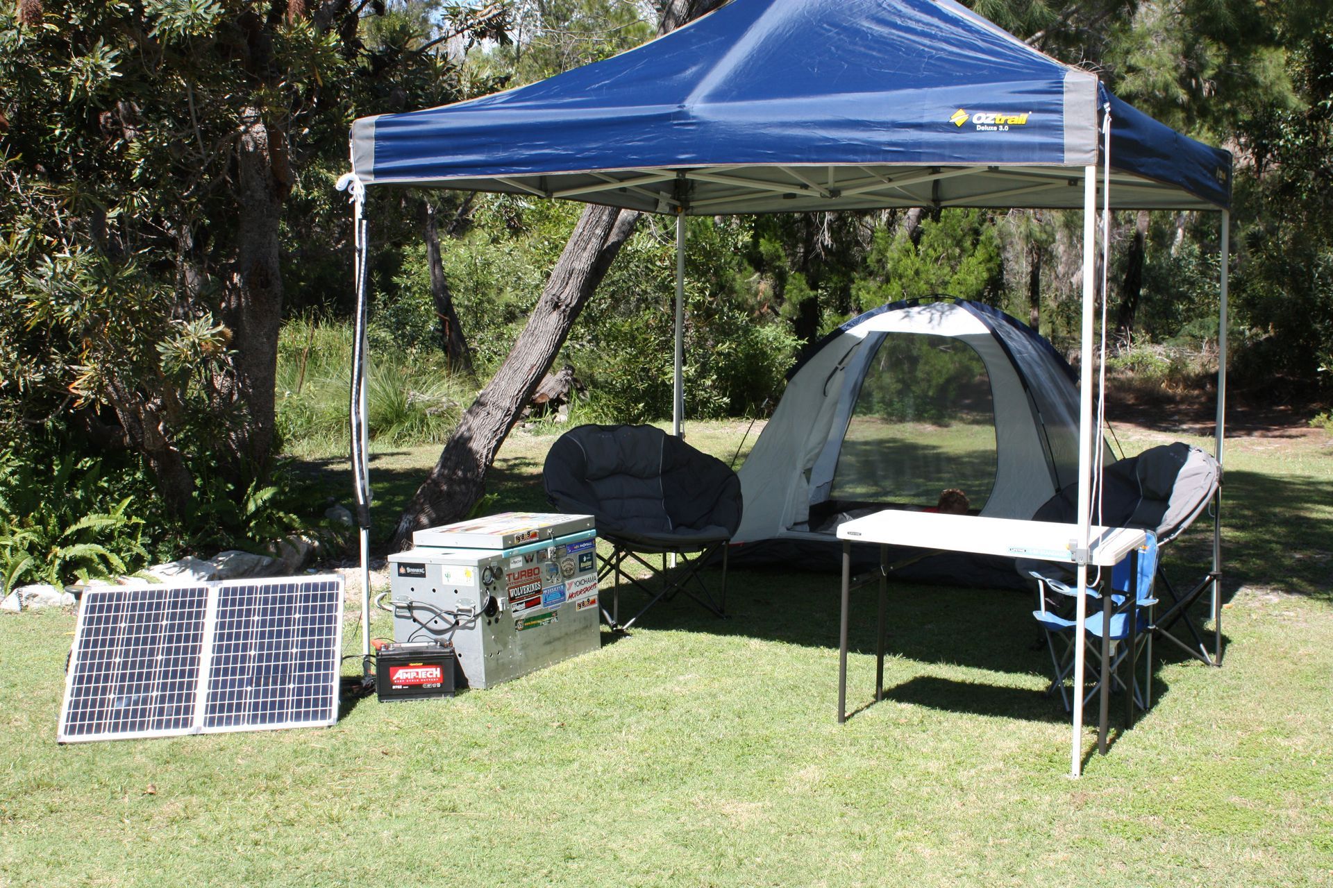 Camping setup with tent, solar panels, and table under a blue canopy on grass. — Rainbow Beach 4x4 Accessories in Rainbow Beach, QLD