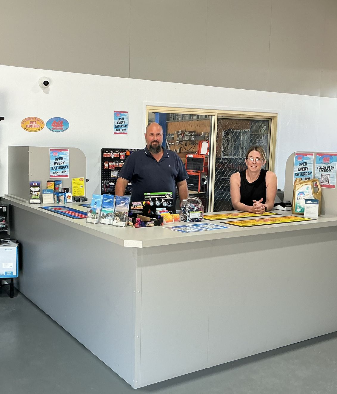 A building with palm trees and parked vehicles on a sunny day. Sign on the left. — Rainbow Beach 4x4 Accessories in Rainbow Beach, QLD