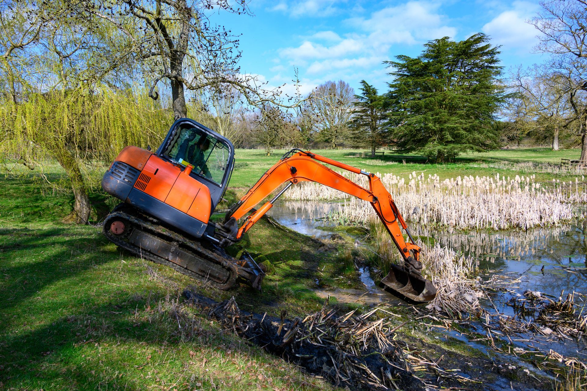 Orange excavator digging in a pond, sunny day.