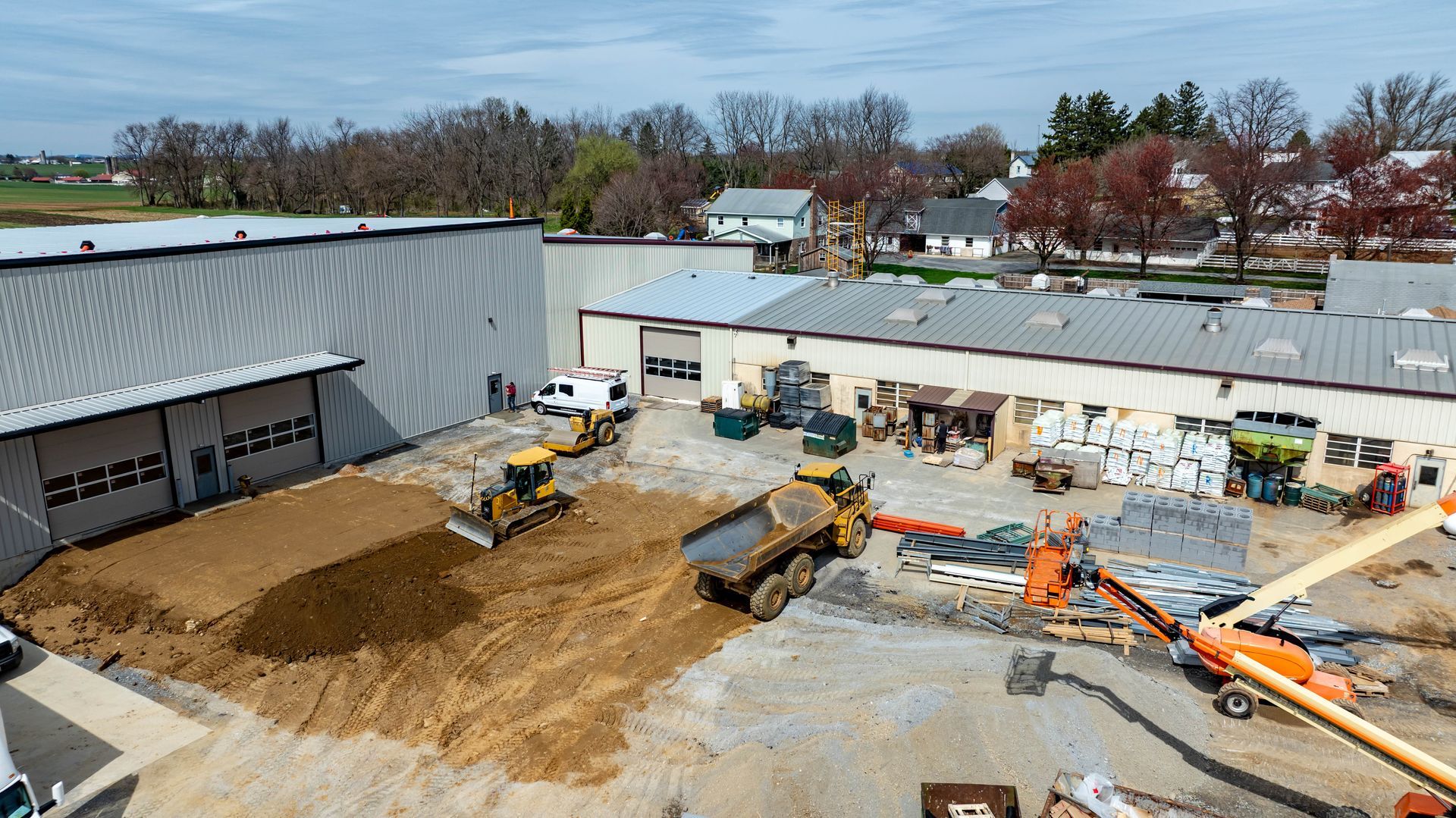 Construction site with heavy machinery like bulldozers, dump truck, and backhoe. Buildings in background.