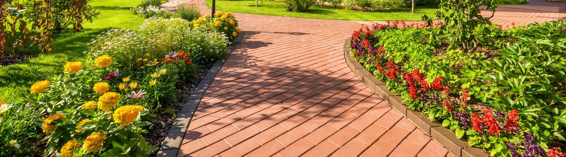 Brick pathway curves through a garden with flower beds and green grass. Brick pathway curves through a garden with flower beds and green grass.