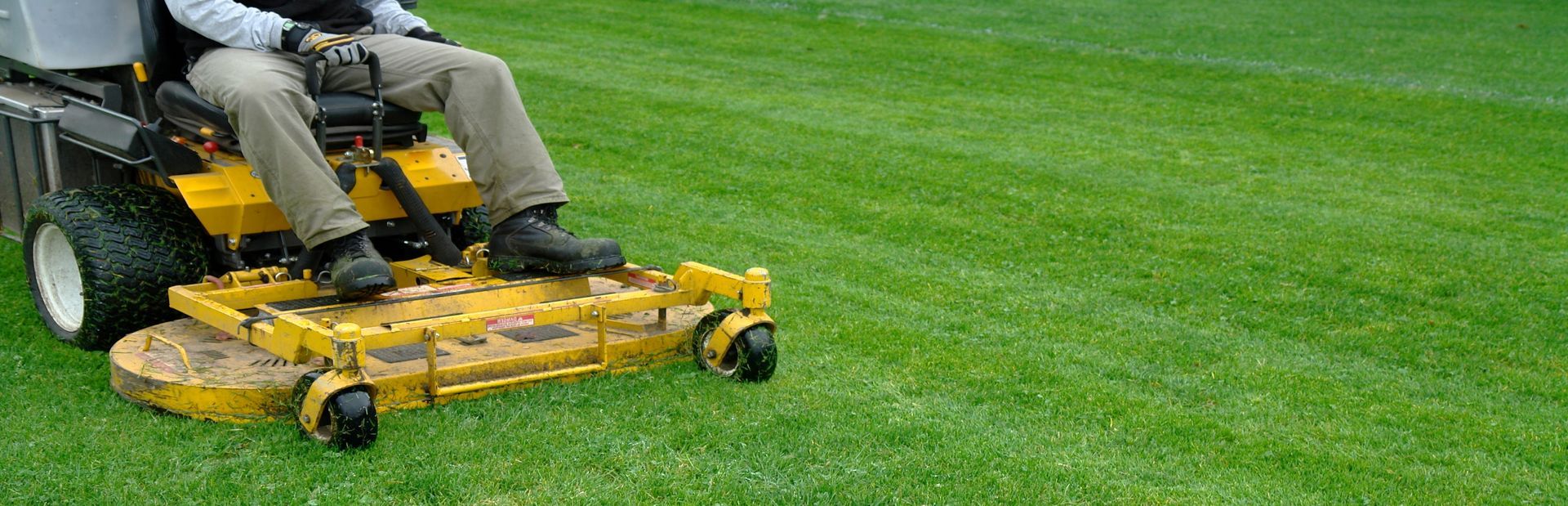 A person on a yellow riding lawnmower cutting green grass in a field. A person on a yellow riding lawnmower cutting green grass in a field.