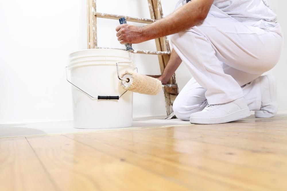 A Man is Kneeling Down Next to a Bucket of Paint and a Paint Roller — Tropical Coats Painting Whitsundays in Cannonvale, QLD
