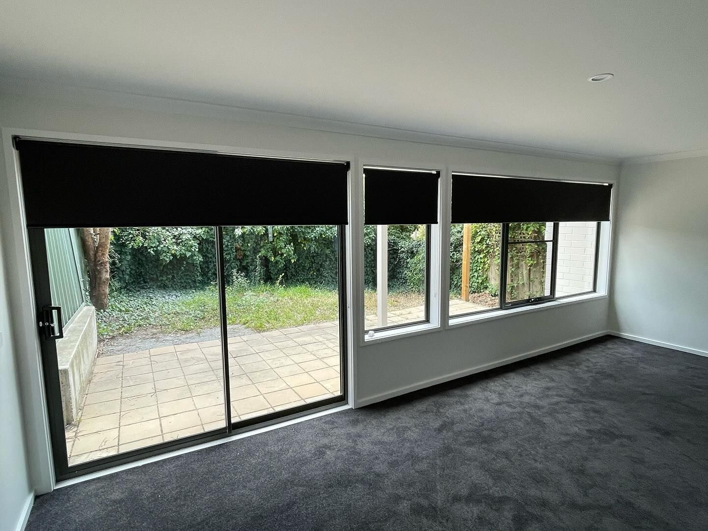 An empty living room with sliding glass doors and black blinds — Elite Window Furnishings In Fyshwick, ACT