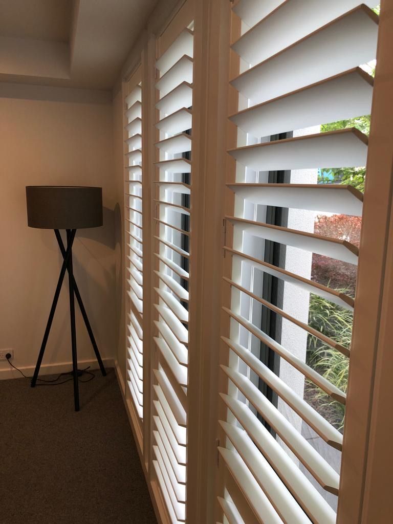 A room with white shutters on the windows and a lamp — Elite Window Furnishings In Fyshwick, ACT
