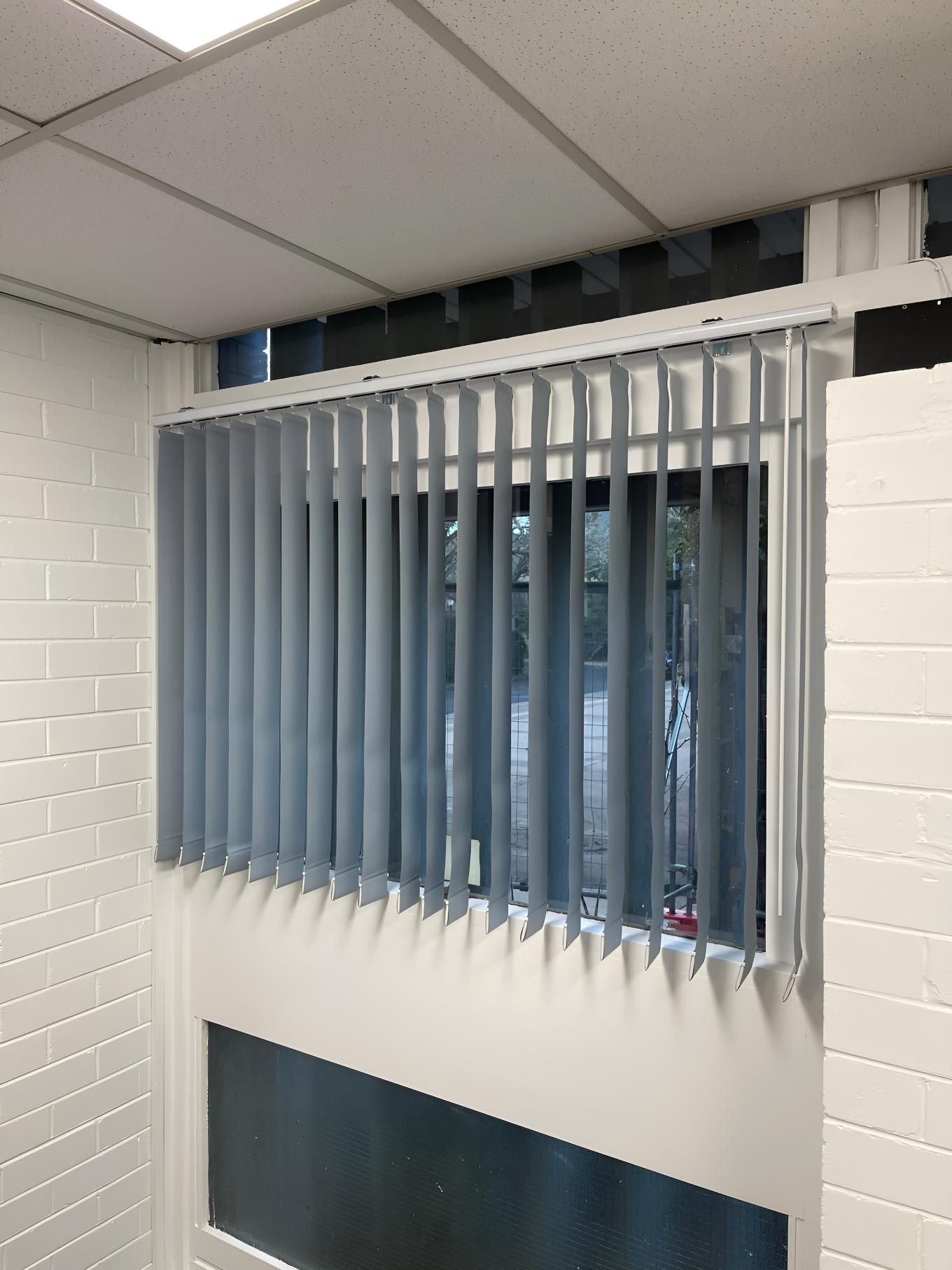 A Window With Vertical Blinds on It and a Brick Wall — Elite Window Furnishings In Gungahlin, ACT