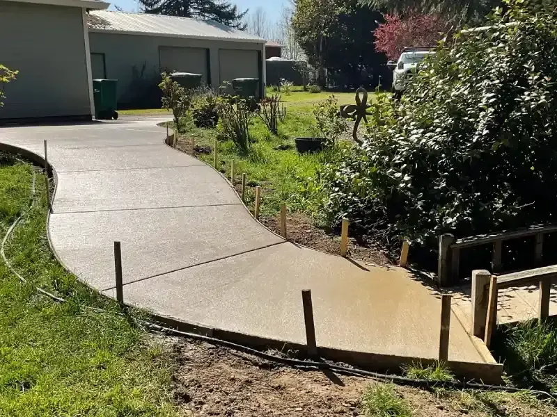 New concrete driveway winding through a green yard, with wooden formwork still in place.