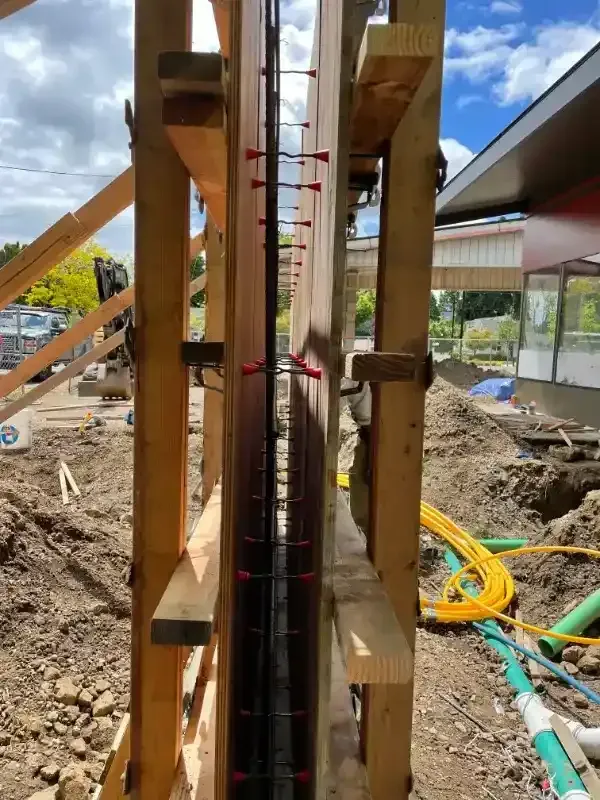 Wooden formwork for a concrete wall with rebar and red spacers in a construction site.