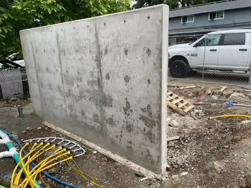 Concrete wall construction site; yellow hoses and white pipes in foreground; truck in background.