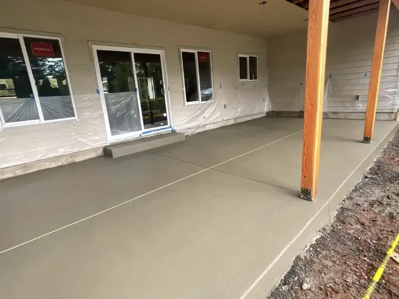 Finished concrete patio outside a house with sliding glass doors and wooden support beams.