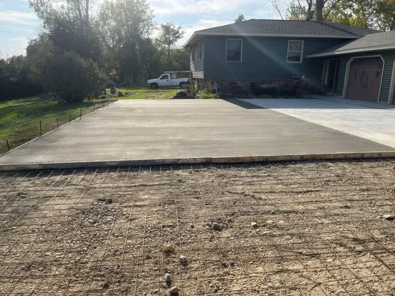 A freshly poured concrete pad next to a house with a driveway.