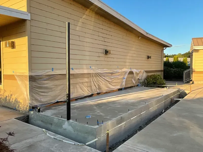 Concrete foundation next to a building, covered in plastic. A black pole stands upright.