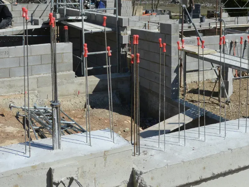 Construction site: concrete foundation with steel rebar extending upward, ready for wall construction.