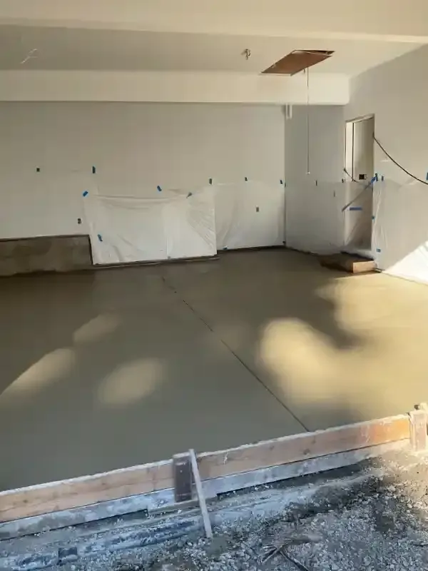 New concrete floor poured in a garage, with white walls and protective sheeting taped up.