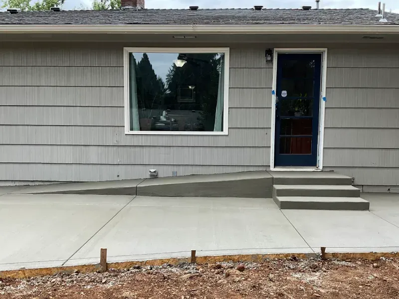 Exterior view of a house with a newly poured concrete ramp and steps leading to the front door.