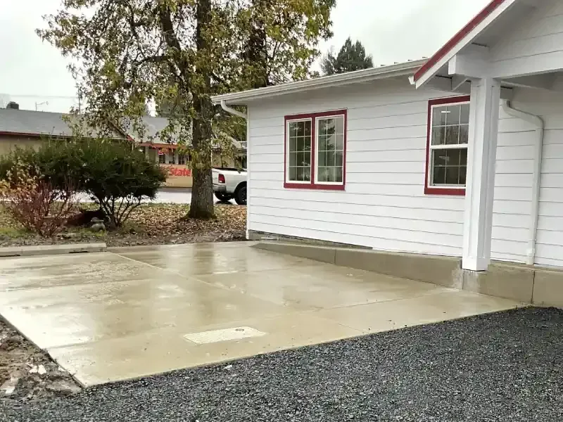 Wet concrete patio in front of a white building with red-trimmed windows and an overcast sky.