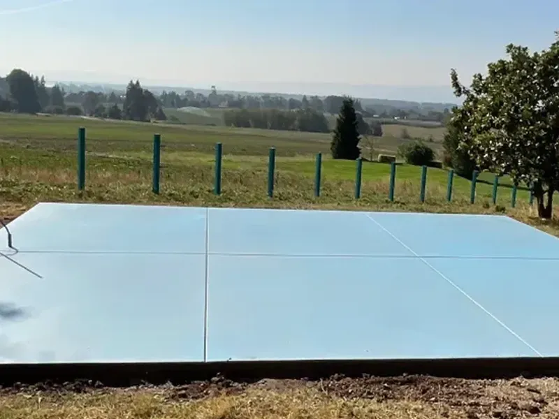 Blue concrete slab in field, with fence and view of green landscape under a clear sky.