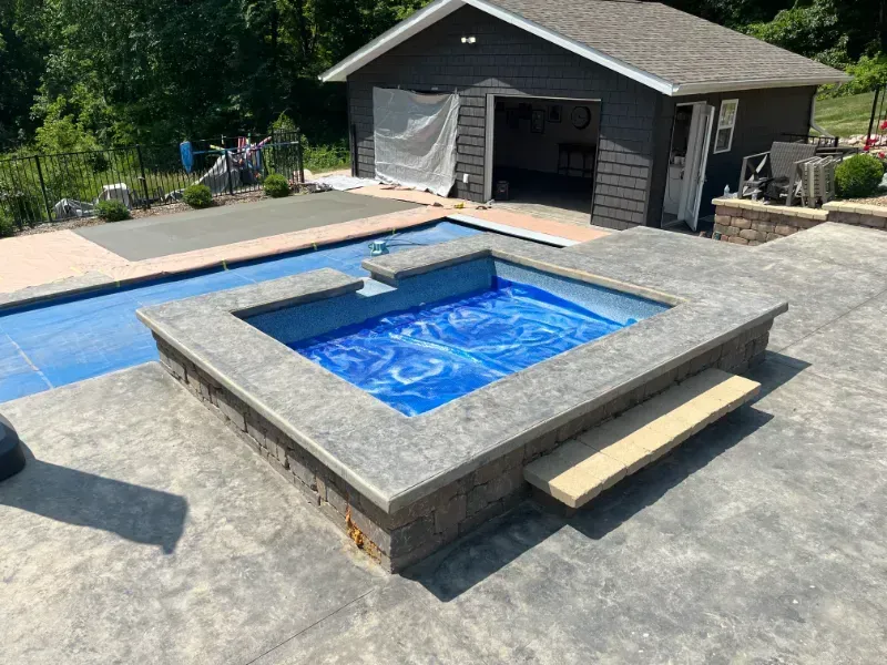 Hot tub with blue water, concrete patio, and garage in the background.