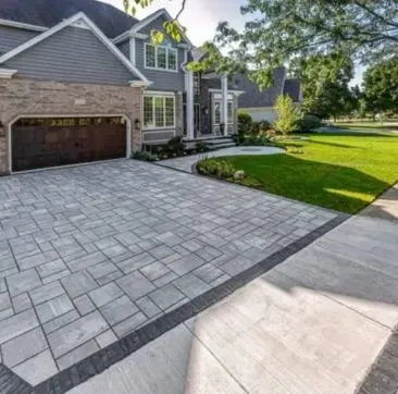 Suburban home with gray paver driveway, green lawn, and a sidewalk.