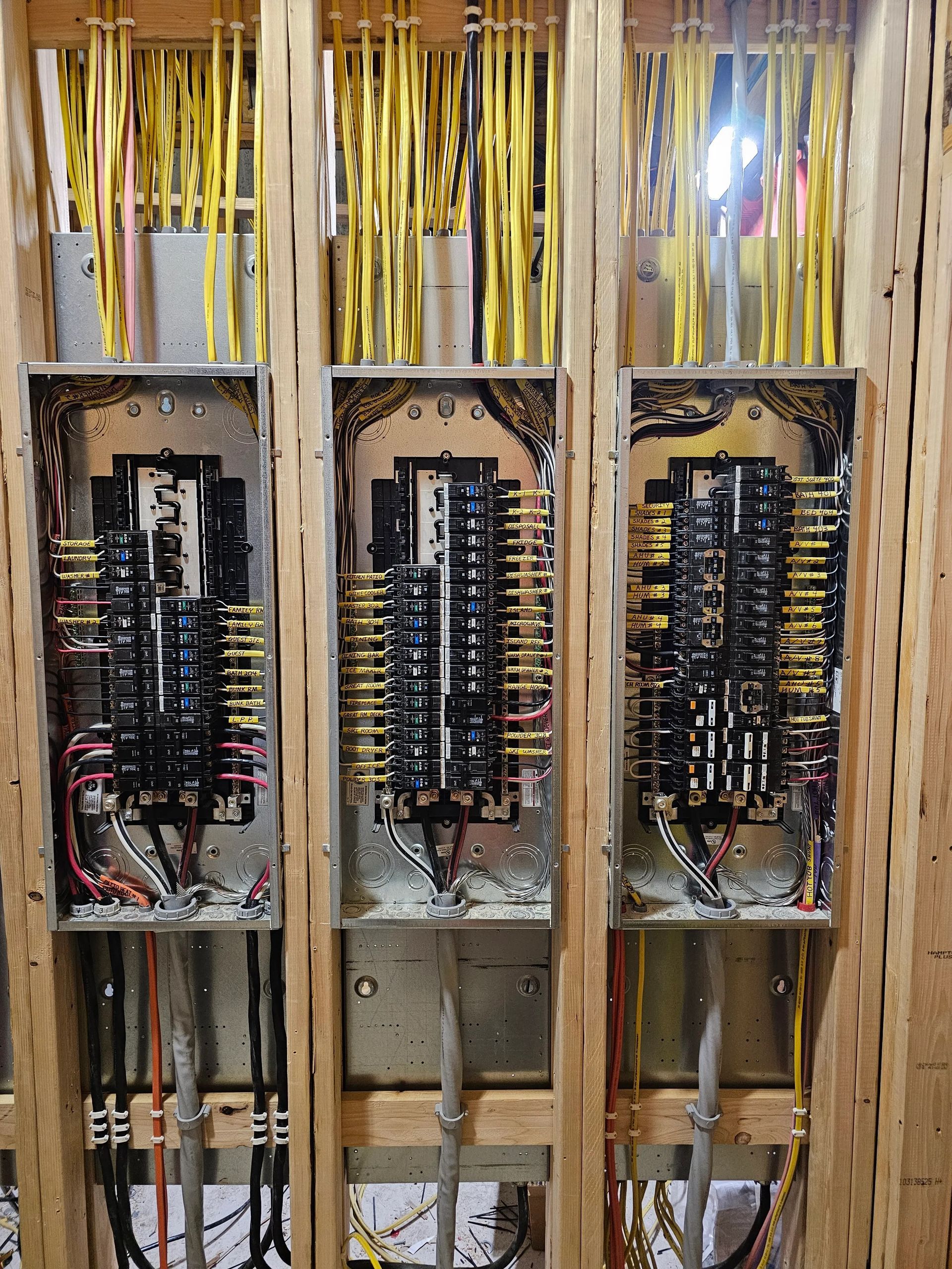 Three open electrical breaker panels with wires and components exposed in a utility room.