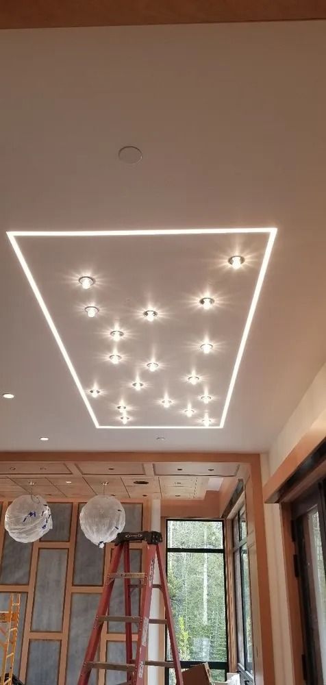 Ceiling with recessed LED border and multiple downlights in an unfinished room with ladders and fans