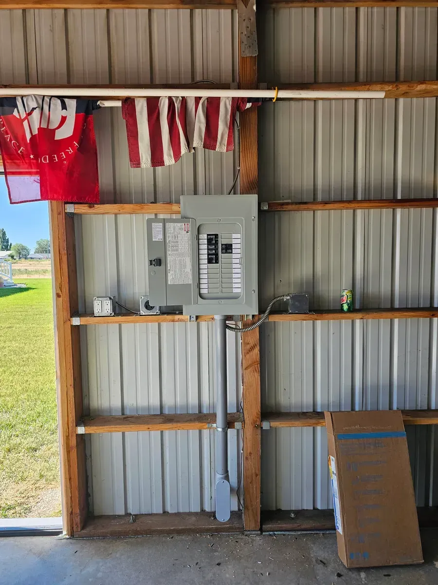 Corrugated metal shed wall with electrical panels, red shirts hanging, and a lawn visible through the open side