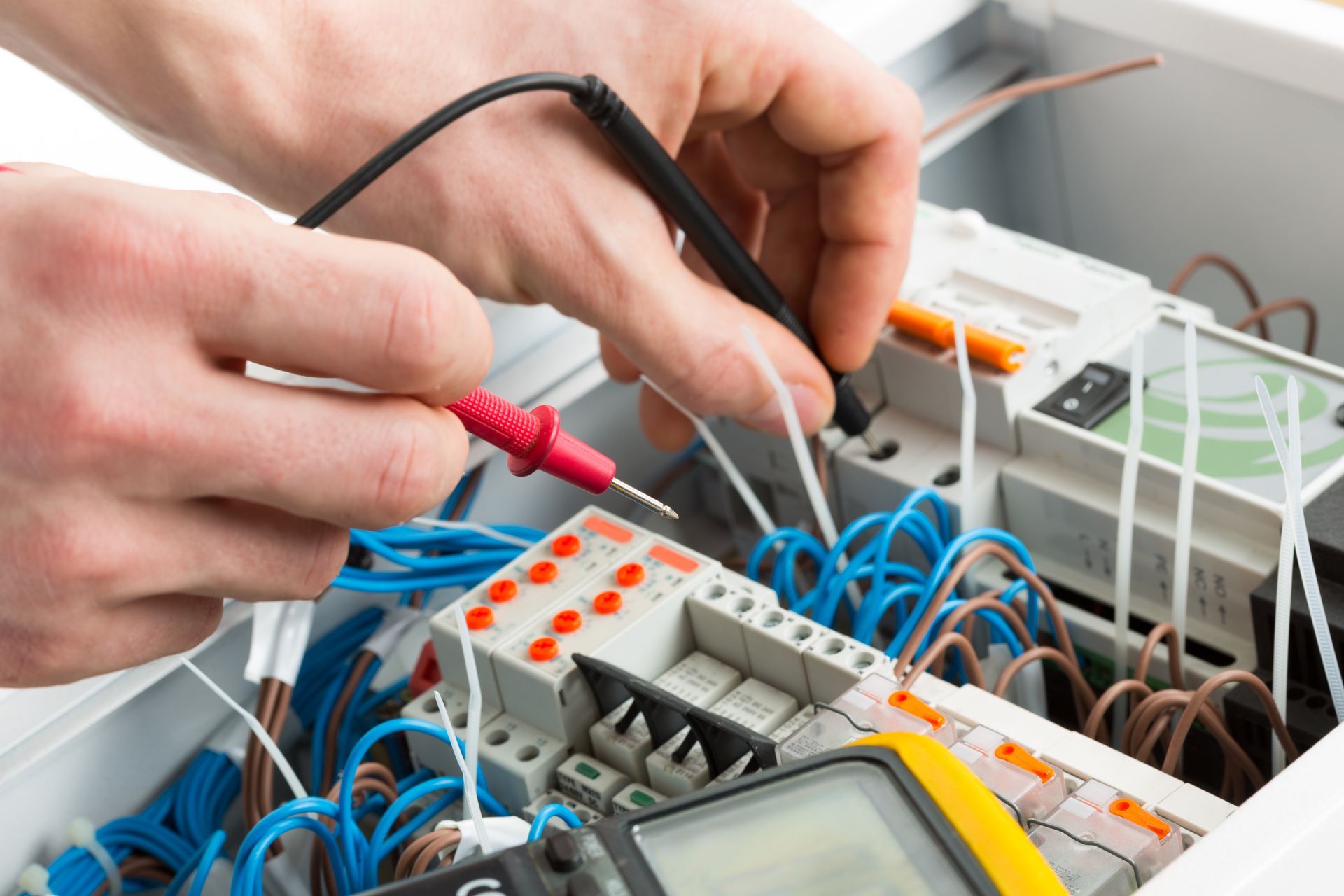 Hands using probes to test electrical wiring in a circuit panel with blue and white cables