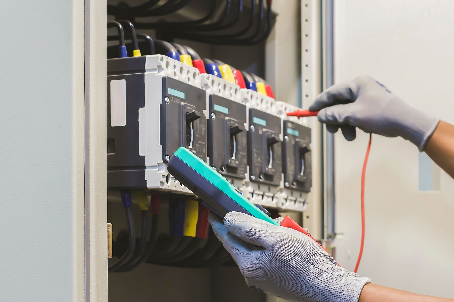Gloved technician testing an electrical breaker panel with a multimeter and probe.