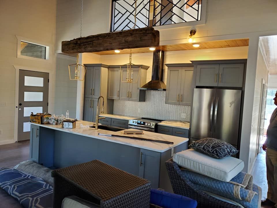 A kitchen with gray cabinets , stainless steel appliances , and a large island in the middle of the room.
