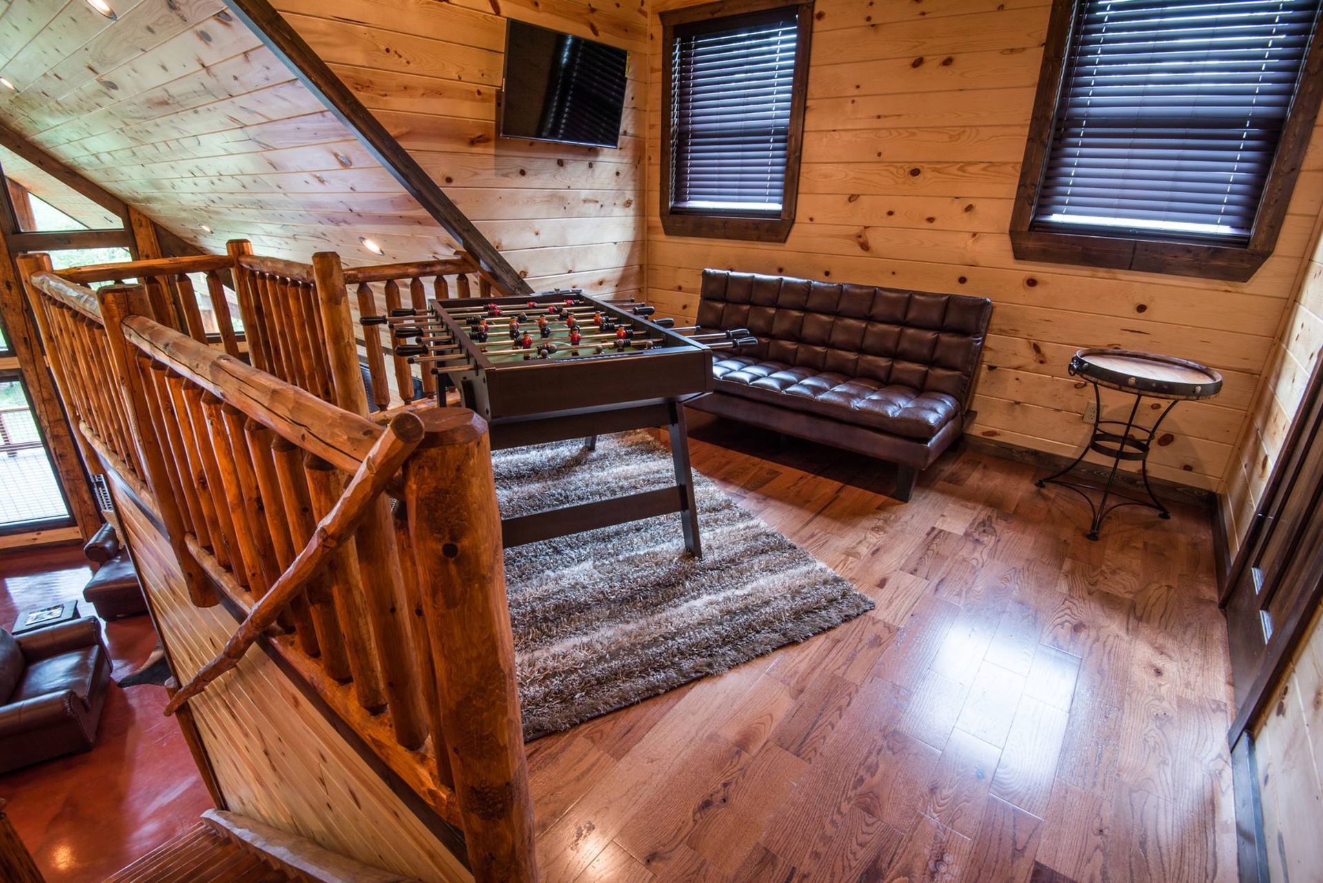 A living room in a log cabin with a foosball table and a couch.