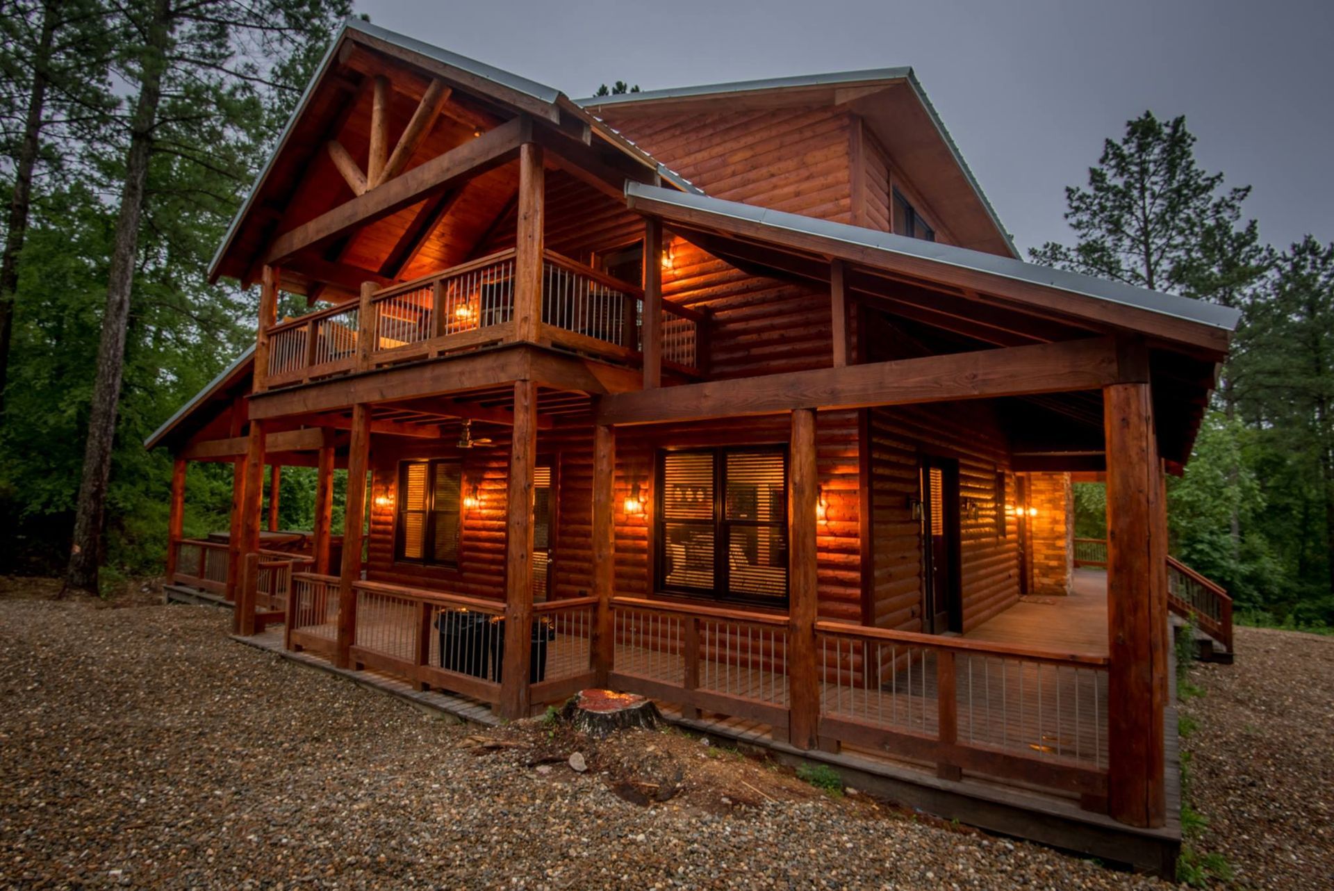 A large log cabin with a large porch in the middle of a forest.