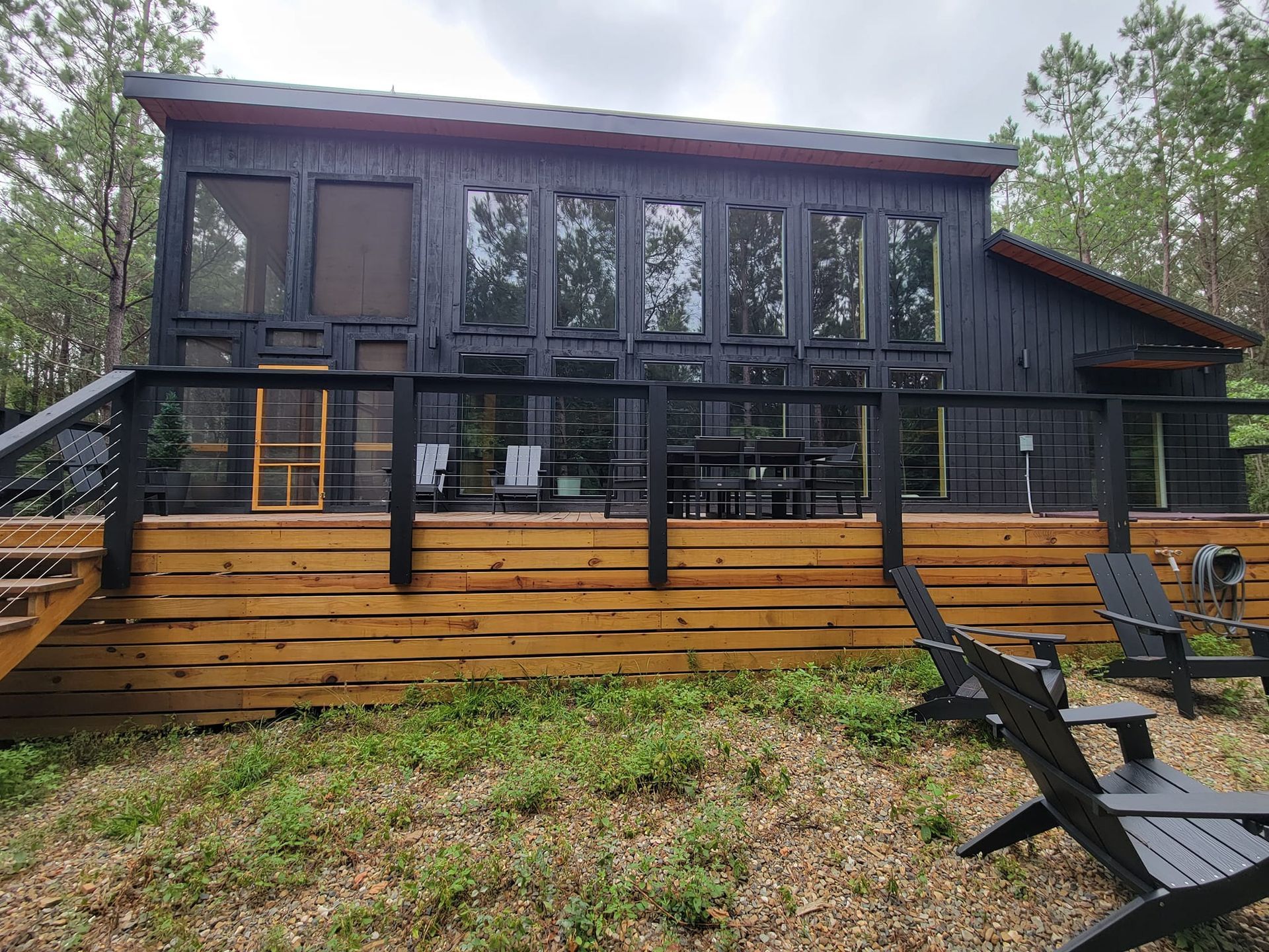 A black house with a wooden deck and chairs in front of it.