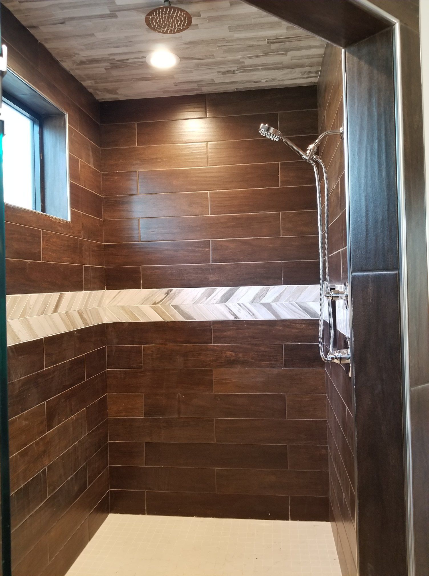 A walk in shower with brown tiles and a shower head.