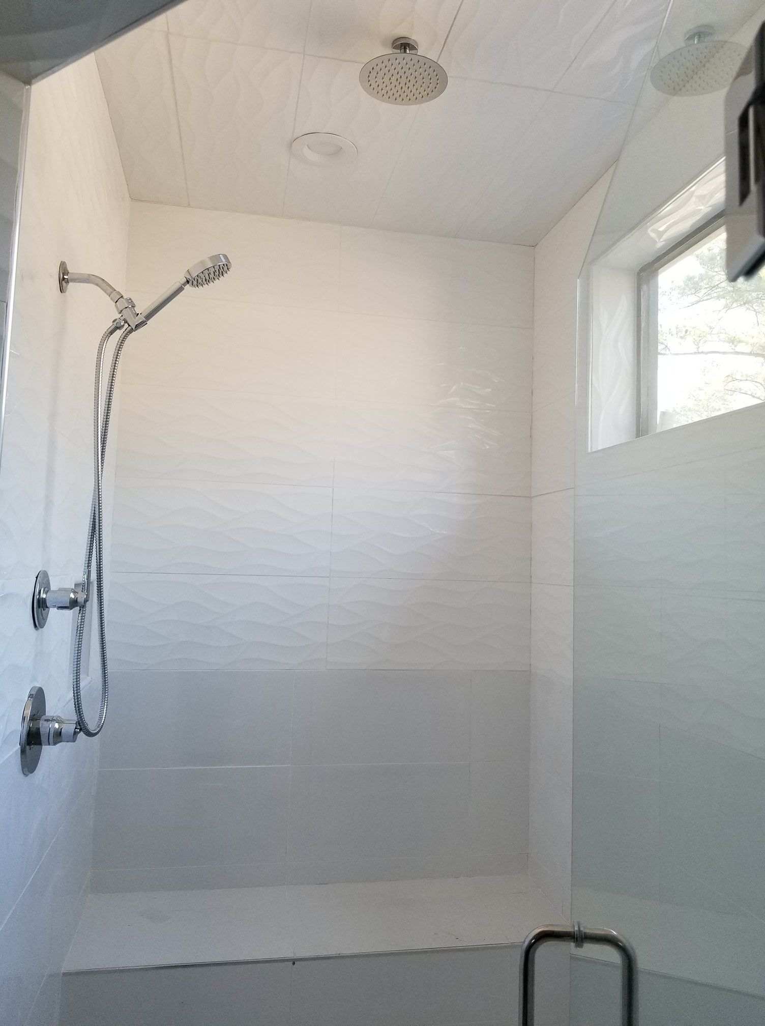 A shower with a shower head and a window in a bathroom.