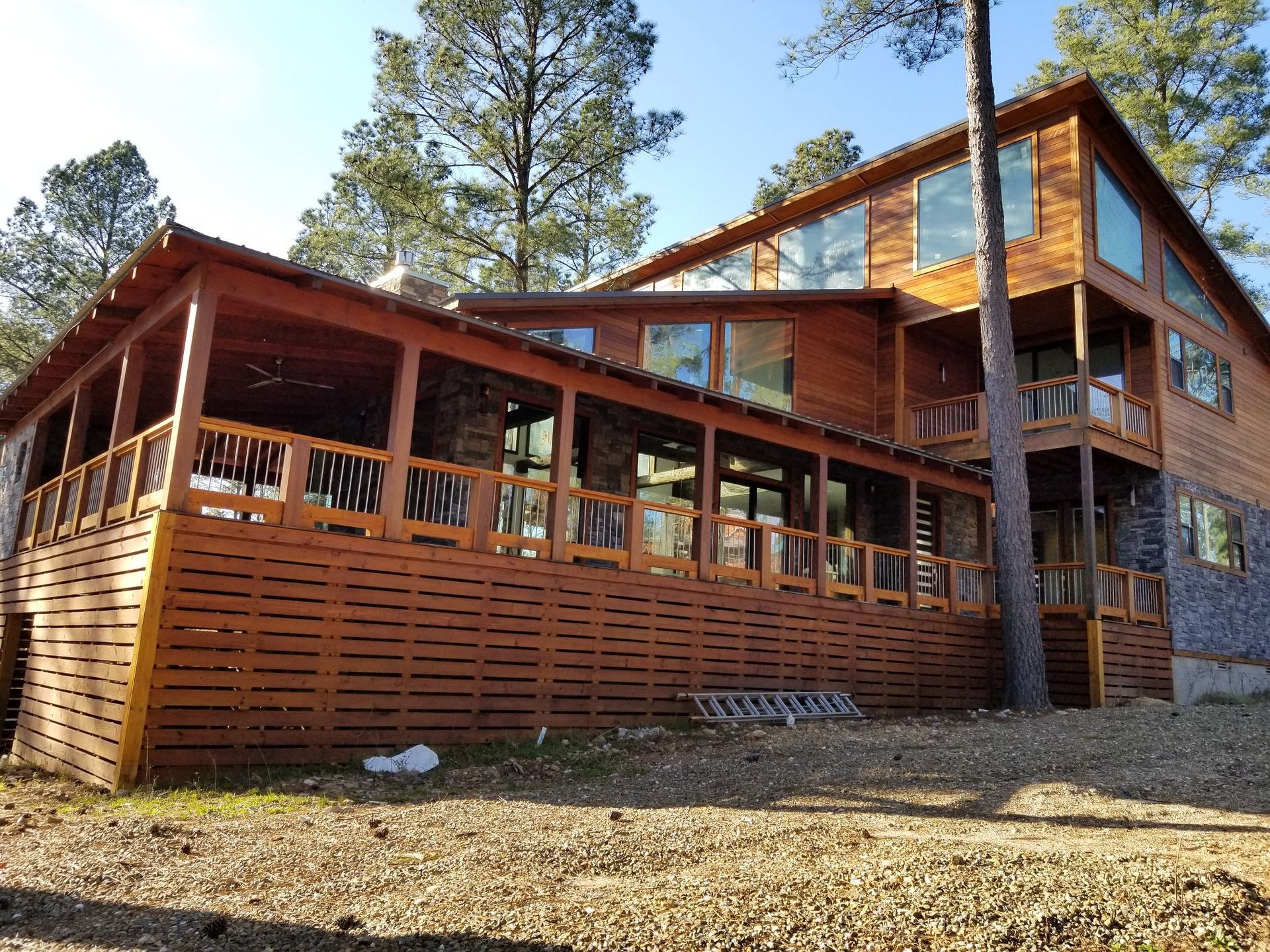 A large wooden house with a large deck is surrounded by trees.