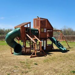 A wooden playground set with a green slide and swings in a field.