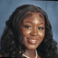 Smiling young Black woman with long wavy black hair, wearing a necklace.