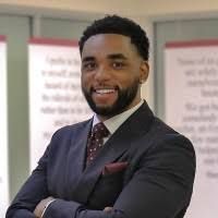 Man in a suit smiles, arms crossed, in front of a blurred background.