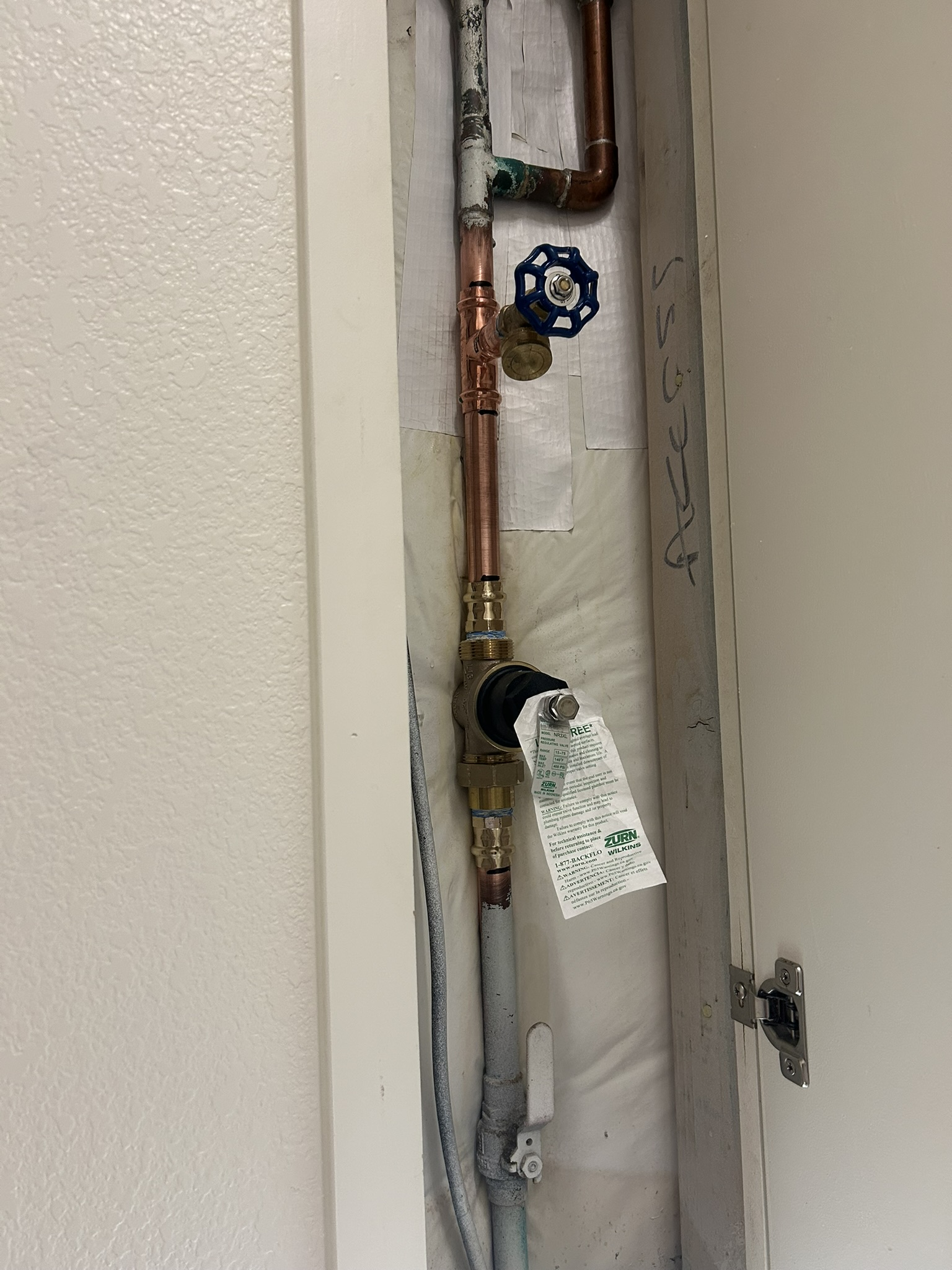 Utility pipes and a blue valve inside a wall access panel with the door open